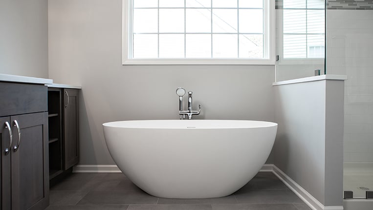 Freestanding white modern bathtub with chrome finishes.