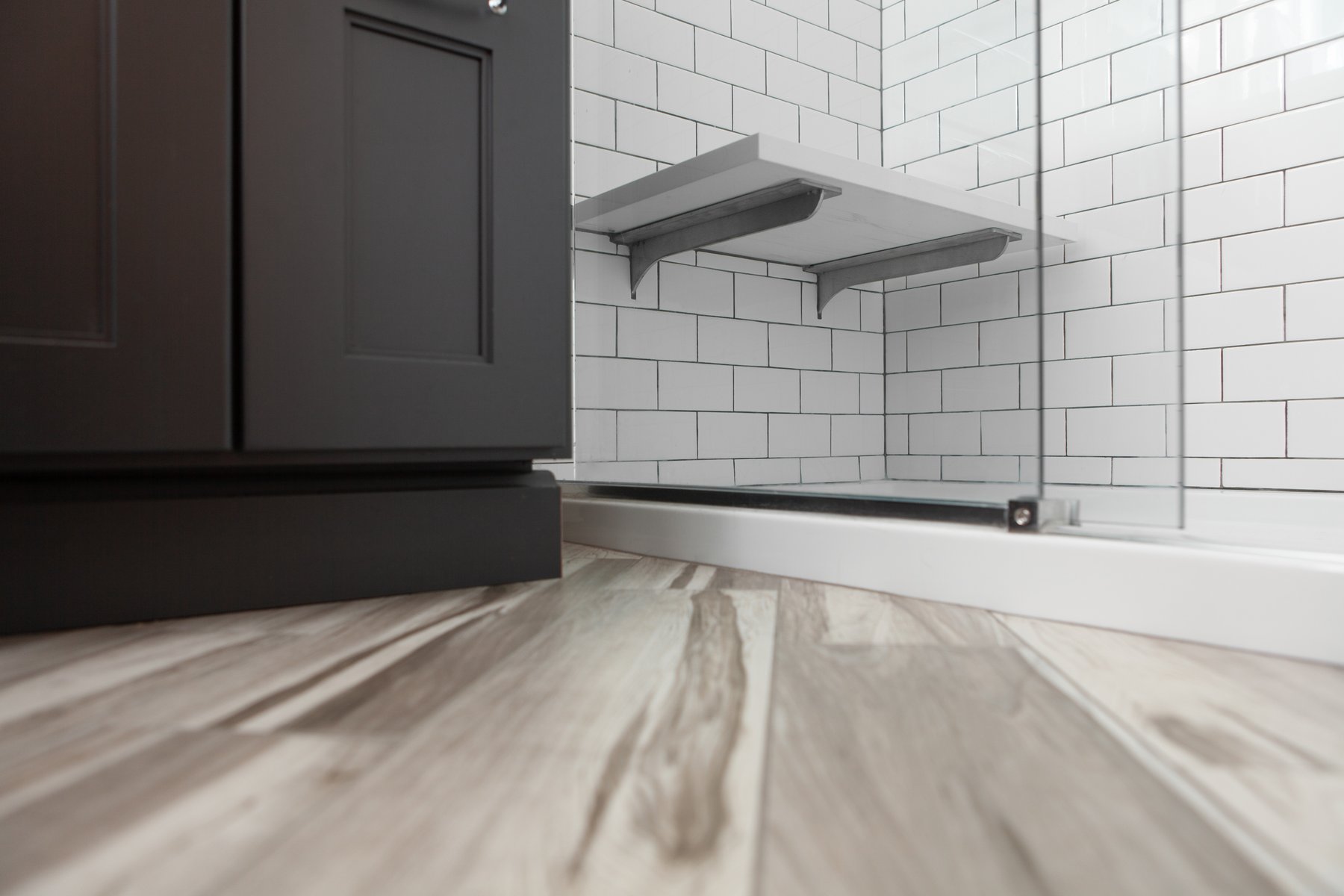 Painted black cabinetry contrasting beautiful hardwood floors and the simplicity of white subway shower tiles