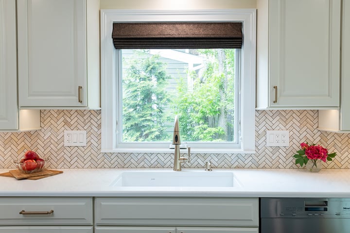 Remodeled kitchen with white conter tops, painted cabinets a basin sink with a window over it.