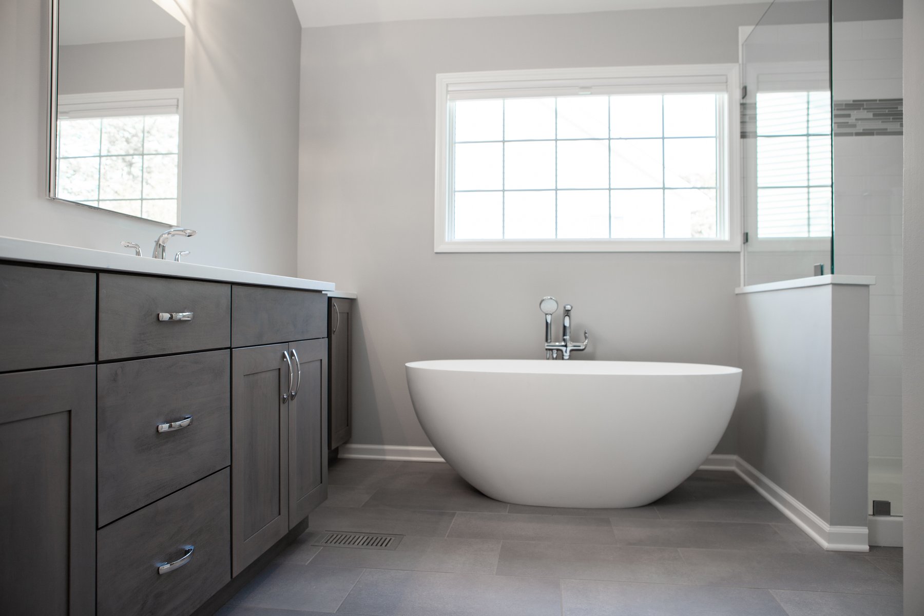 Beautiful modern bathroom remodel in Lake Zurich with natural gray cabinets, chrome finishes and white tub.
