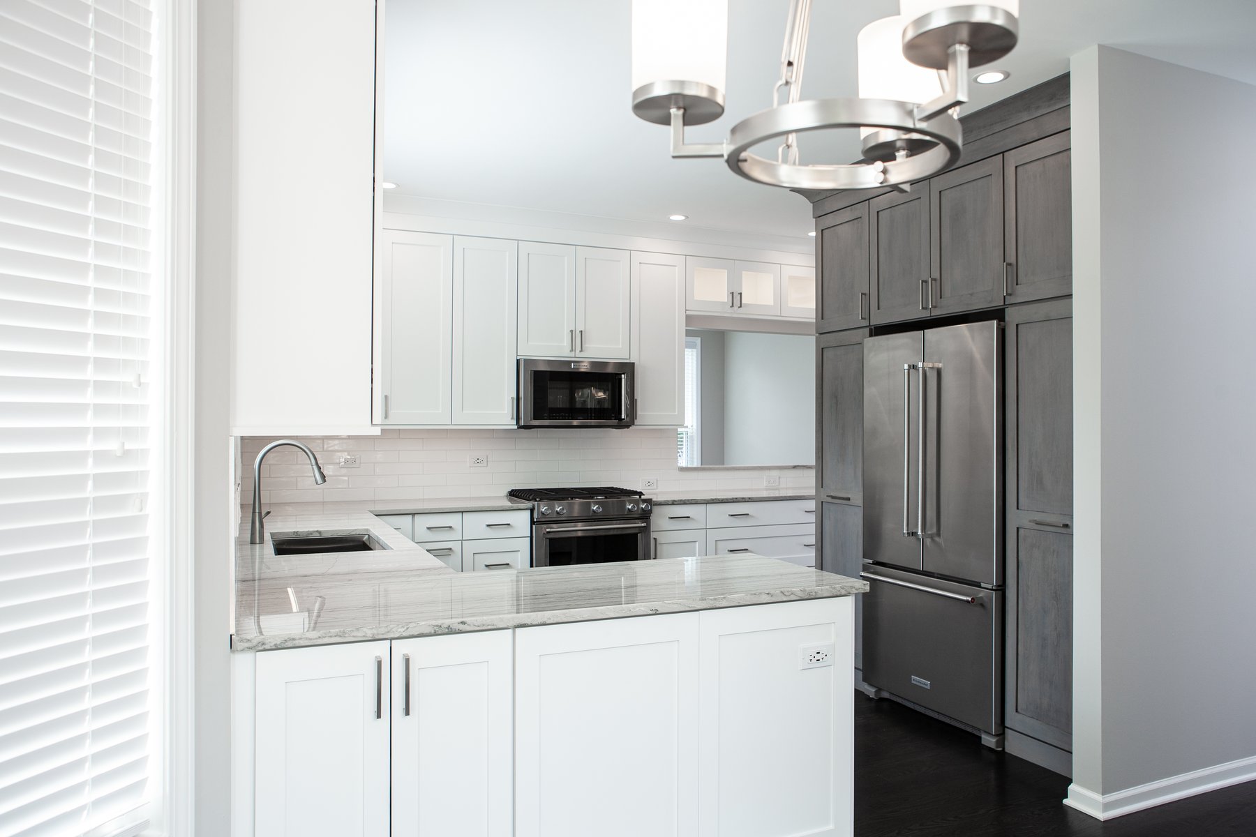 Beautiful modern kitchen remodel in Lake Zurich with natural wood floors, white cabinets and wooden accent cabinetry around the refrigerator.