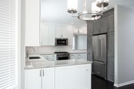 Beautiful modern kitchen remodel in Lake Zurich with natural wood floors, white cabinets and wooden accent cabinetry around the refrigerator.