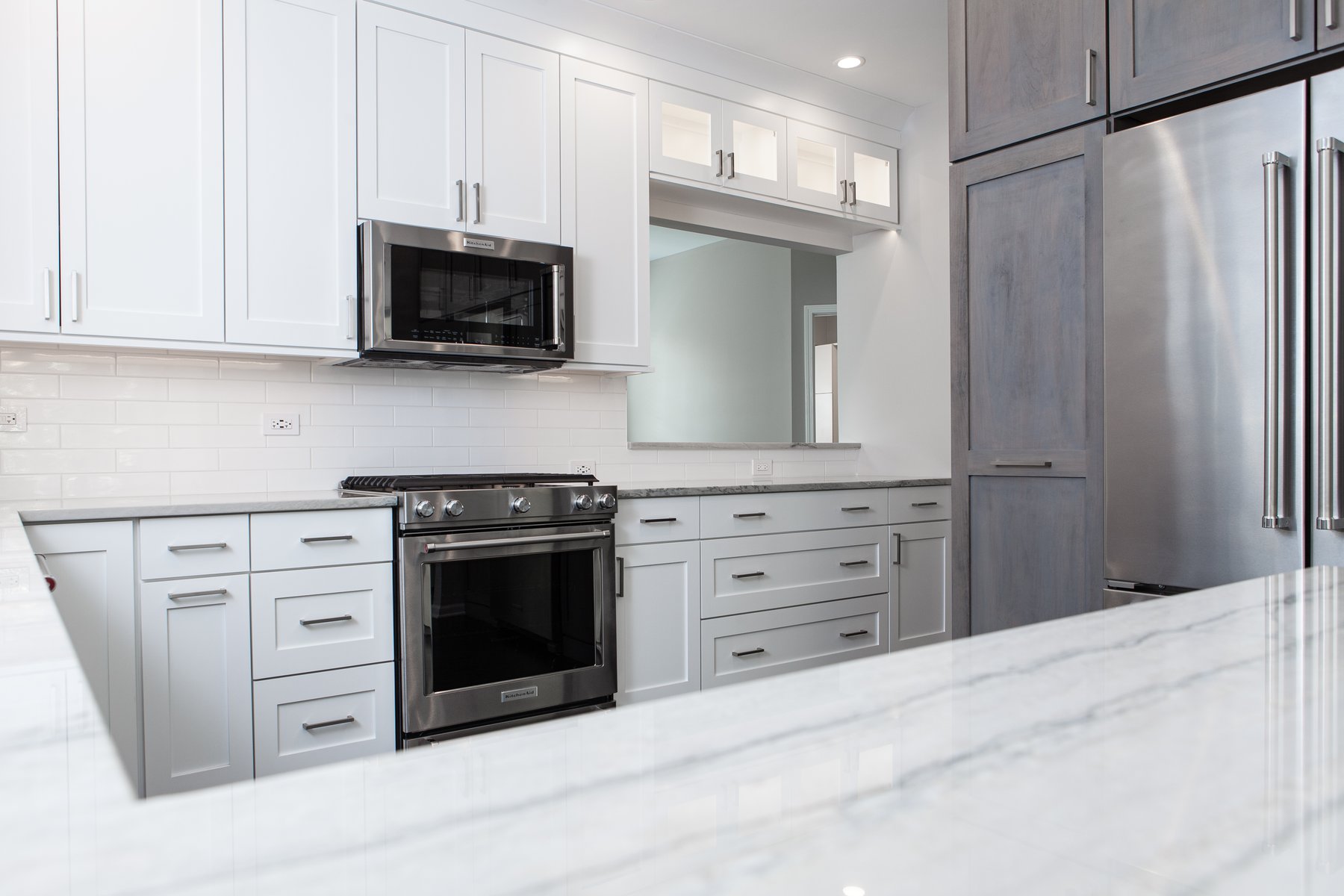 Beautiful modern kitchen remodel in Lake Zurich with natural wood floors, white cabinets and wooden accent cabinetry around the refrigerator.