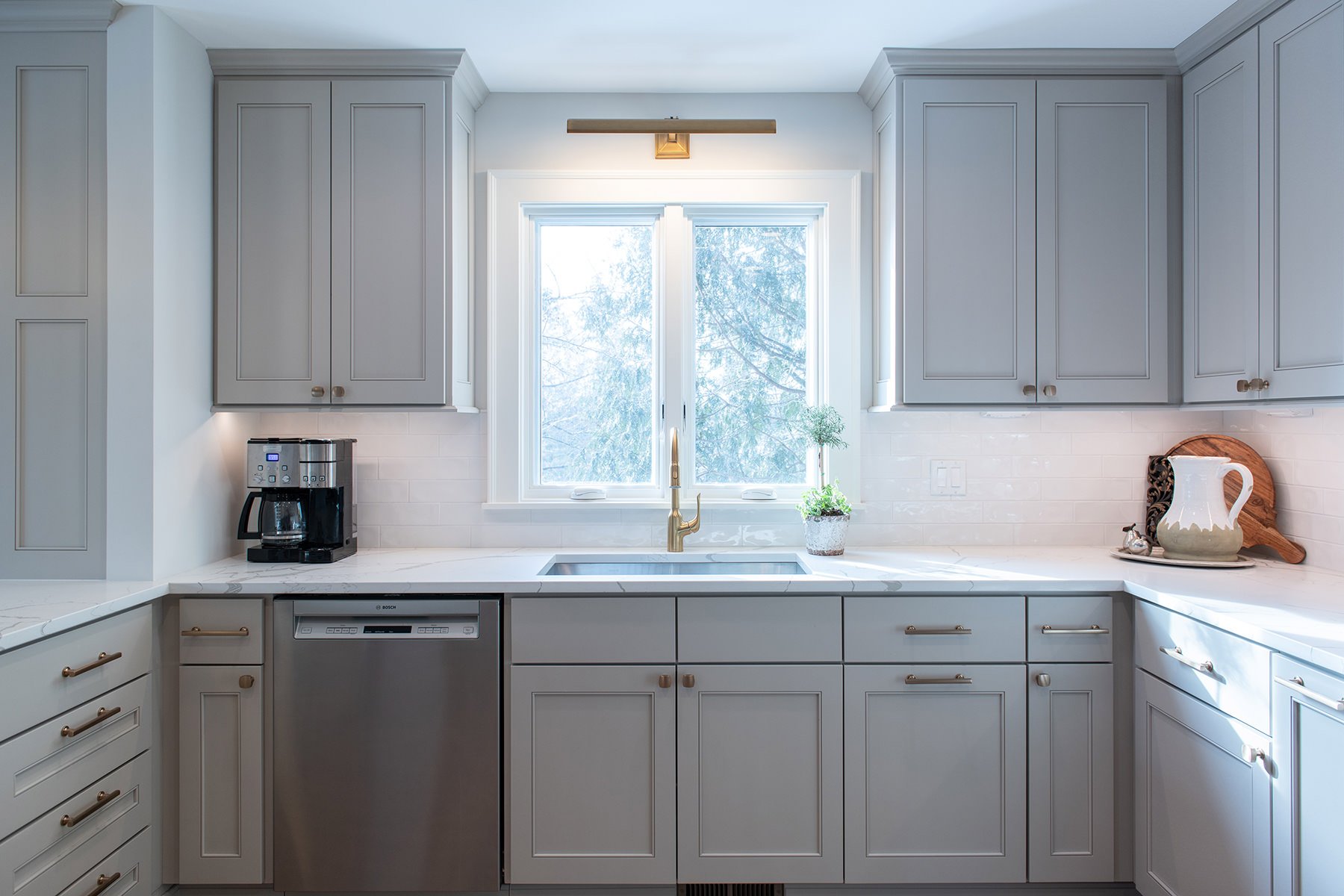 Kitchen renovation with gray painted cabinets, gold hardware, white marble countertops and a backsplash with white subway tile.