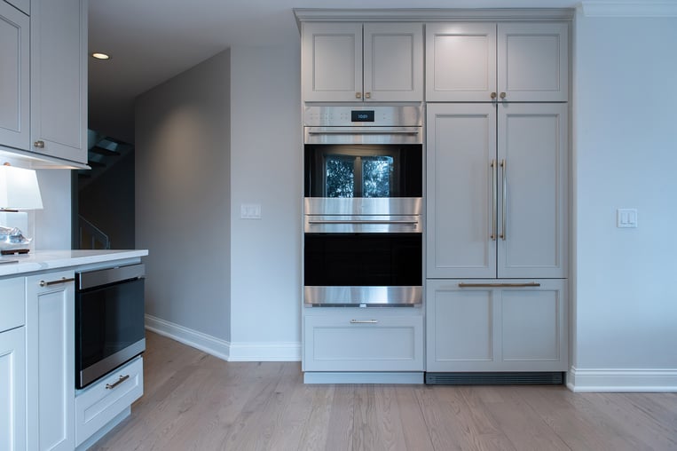 Remodeled home kitchen with white counter tops, light gray custom kitchen cabinets and champagne bronze kitchen hardware.