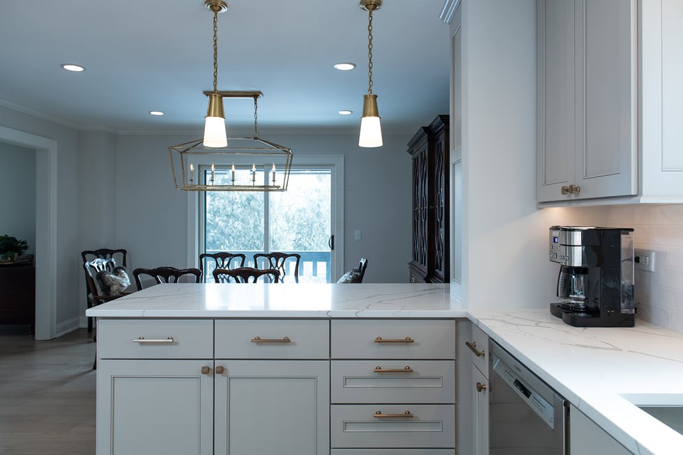 Remodeled home kitchen with white counter tops, light gray custom kitchen cabinets and champagne bronze kitchen hardware.