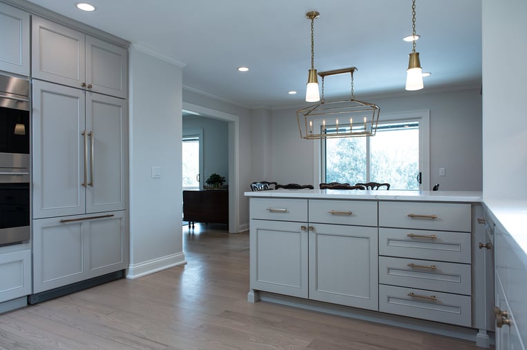 Remodeled home kitchen with white counter tops, light gray custom kitchen cabinets and champagne bronze kitchen hardware.