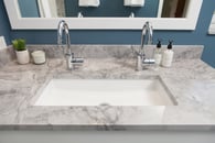 Classic style in this hall bath remodel in Libertyville, Illinois with blue walls, white mirror, chrome hardware and gray countertops including double faucets with a single basin sink.