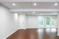 Remodeled basement with hardwood flooring, light gray wall paint and lots of windows throughout.