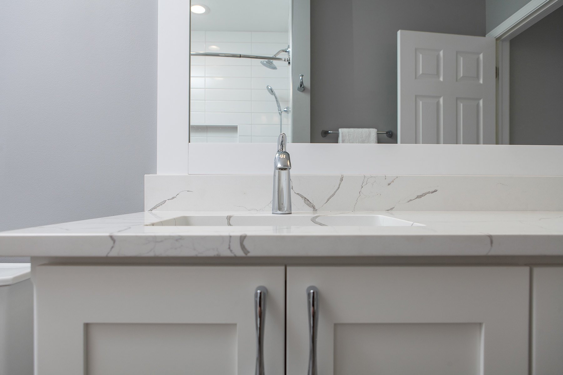 remodeled home bathroom with white cabinetry, light gray countertops and chrome finishes