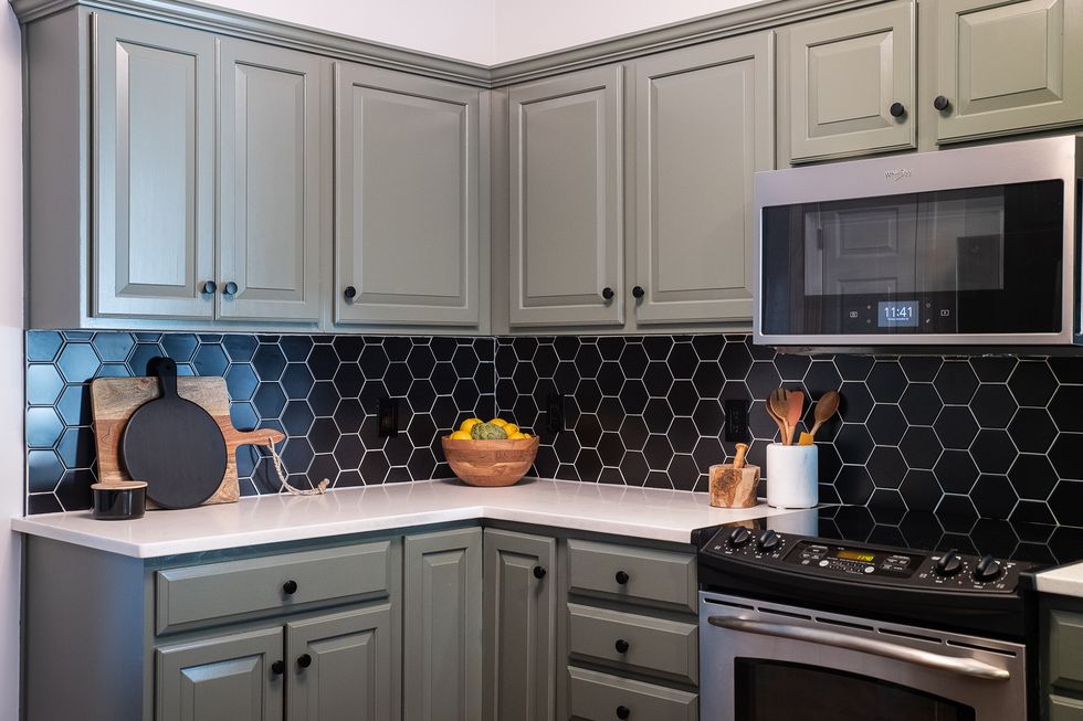 Muted green kitchen colors on painted kitchen cabinets with black hexagon tile backsplash.