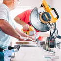 Two men working with saws to cut a piece of wood on the interior of a home.