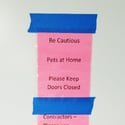 Taped sign to a door that reads, "Be cautious. Pets at home. Please keep doors closed."