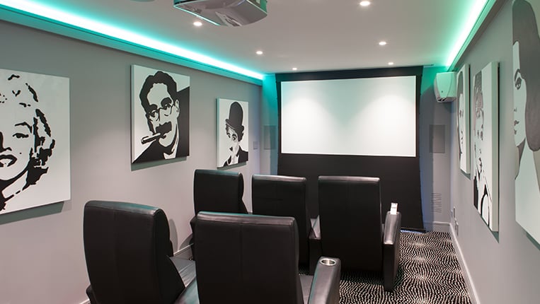 Basement home theater with gray walls, black theater seating, large projection screen and classic black and white movie posters on the walls.