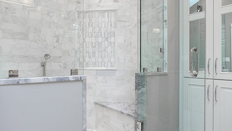 Large shower with glass door and marble gray and white tiles.