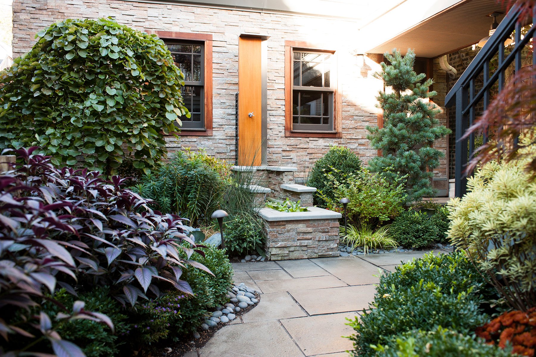 Patio and garden remodel in Lincoln Park, IL with hardscaping patio, fresh shrubs and a beautiful stone fountain from BDS Design Build Remodel.