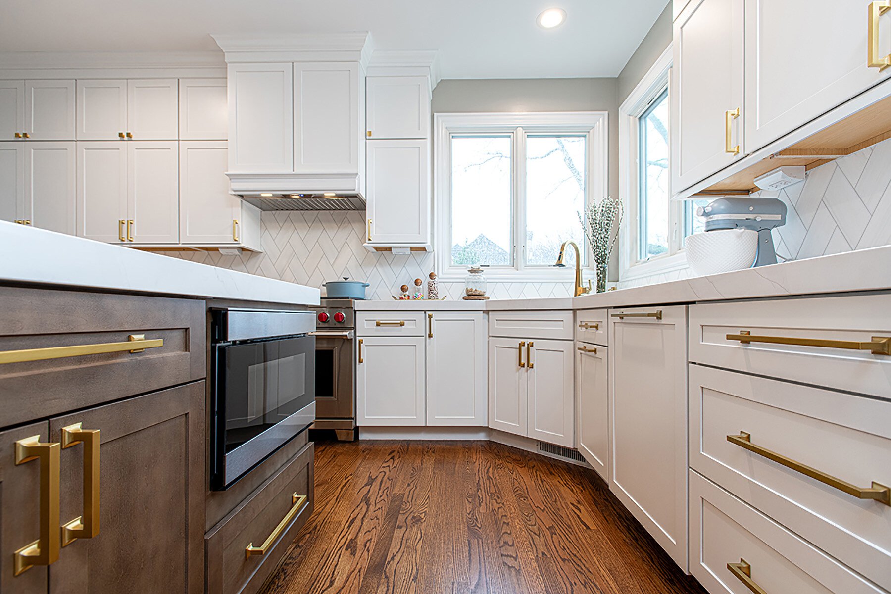 Modern kitchen with white cabinets and gold hardware. Wood floors and a dark wood stained island.