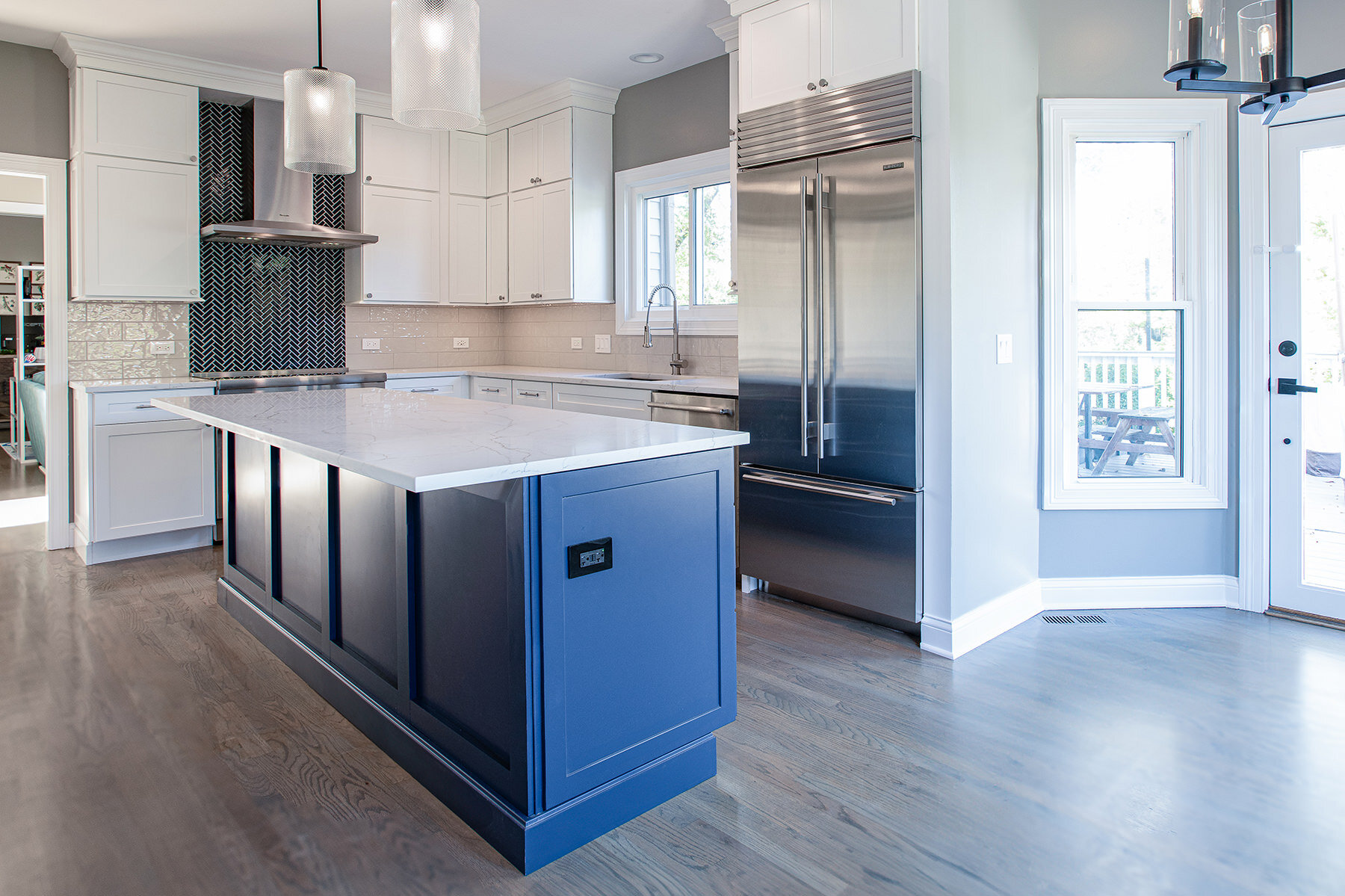 Remodeled kitchen with natural wood floors, blue kitchen island and white cabinetry with white countertops, stainless steal appliances and glass pendant lights.