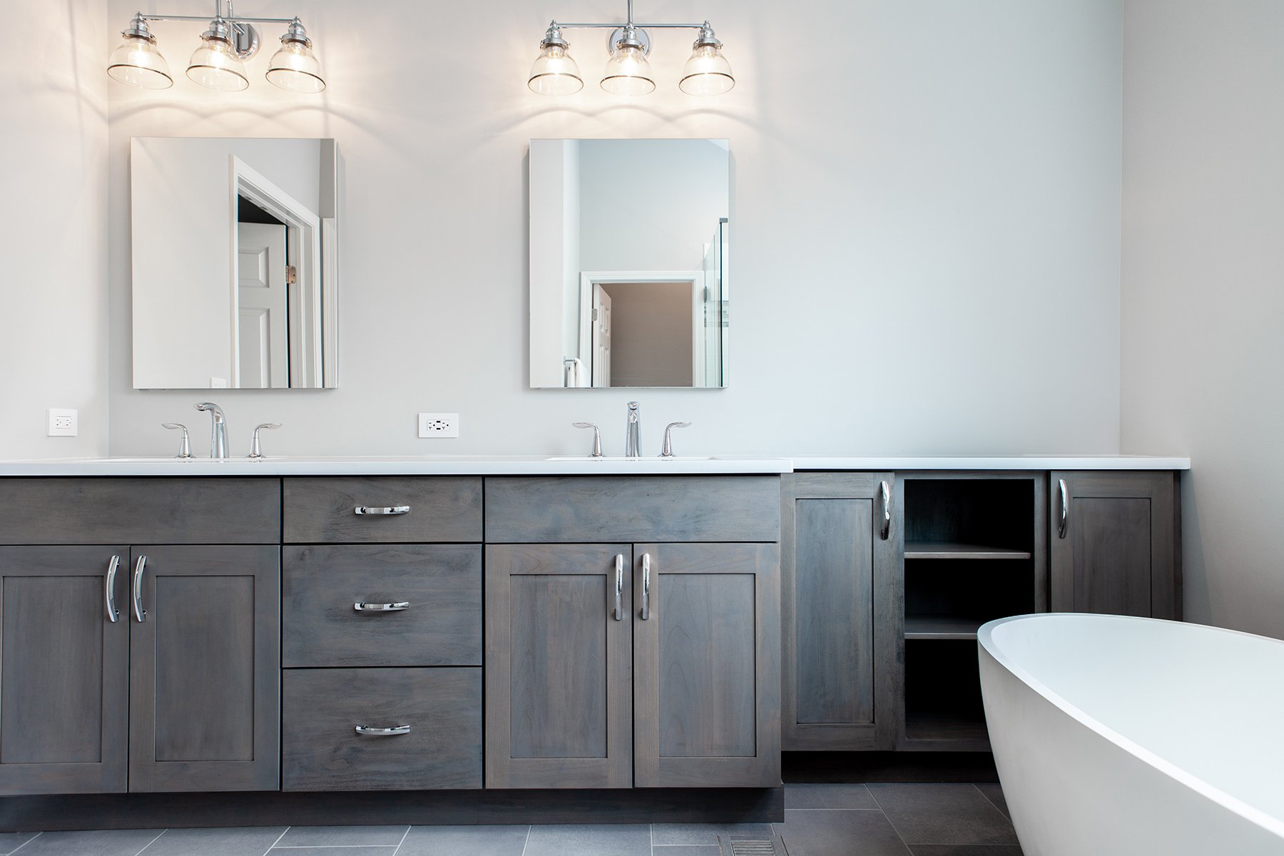 Modern bathroom with wooden cabinets, white walls, double sink with mirrors and a tub on the side of the room..