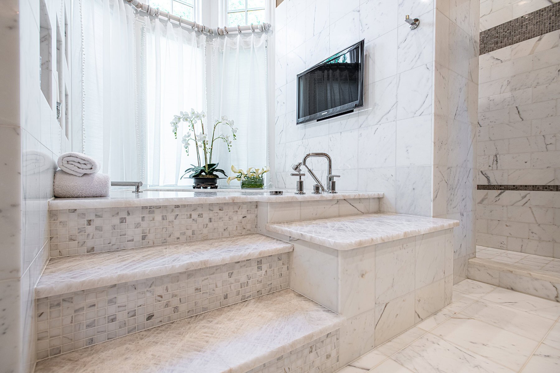 elevated primary bath tub with tiled steps and a tiled wall