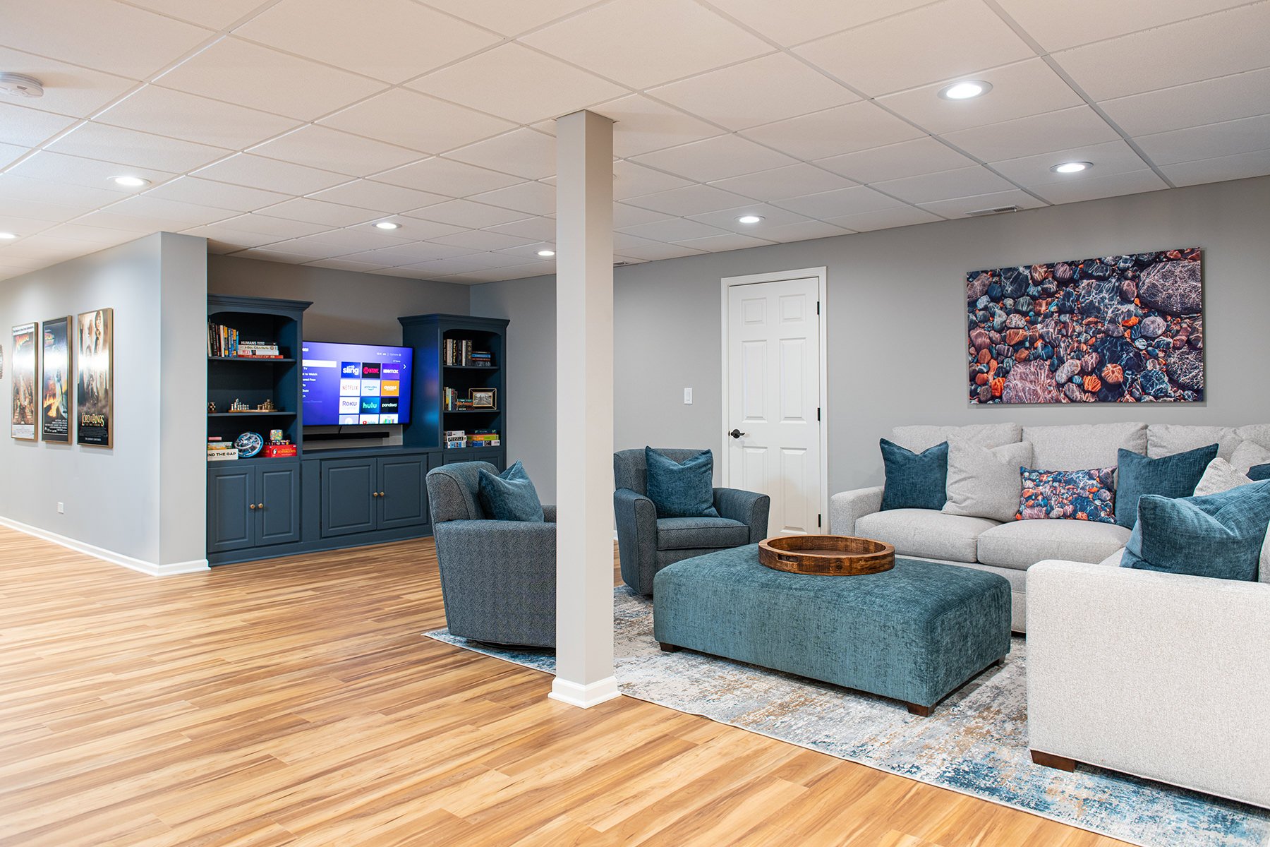 Basement with natural wood floors, gray walls and white ceiling, as well as custom blue cabinetry and recessed lighting.