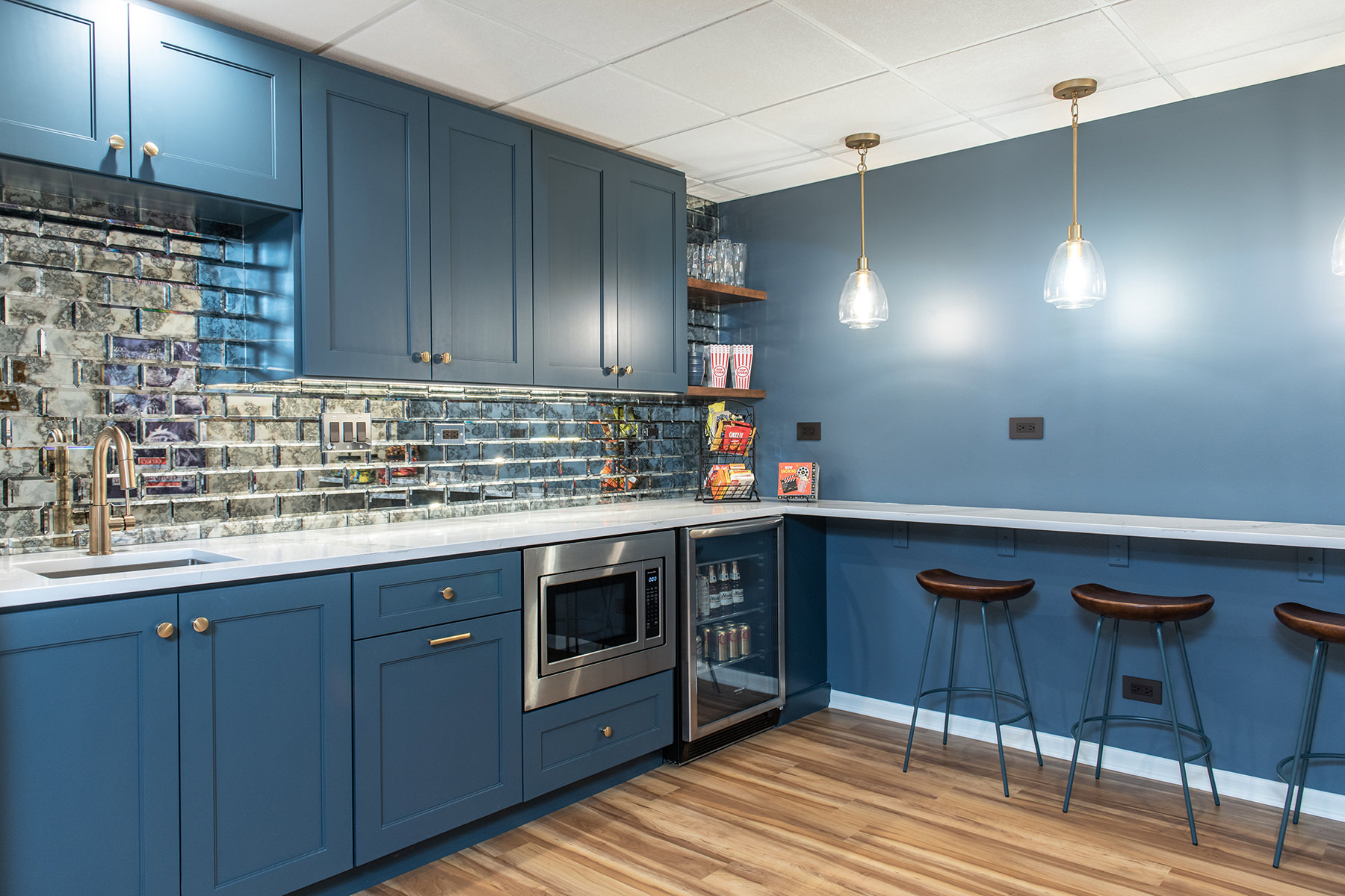 Basement kitchen with wood floors, blue cabinets and mirrored backsplash tiles.