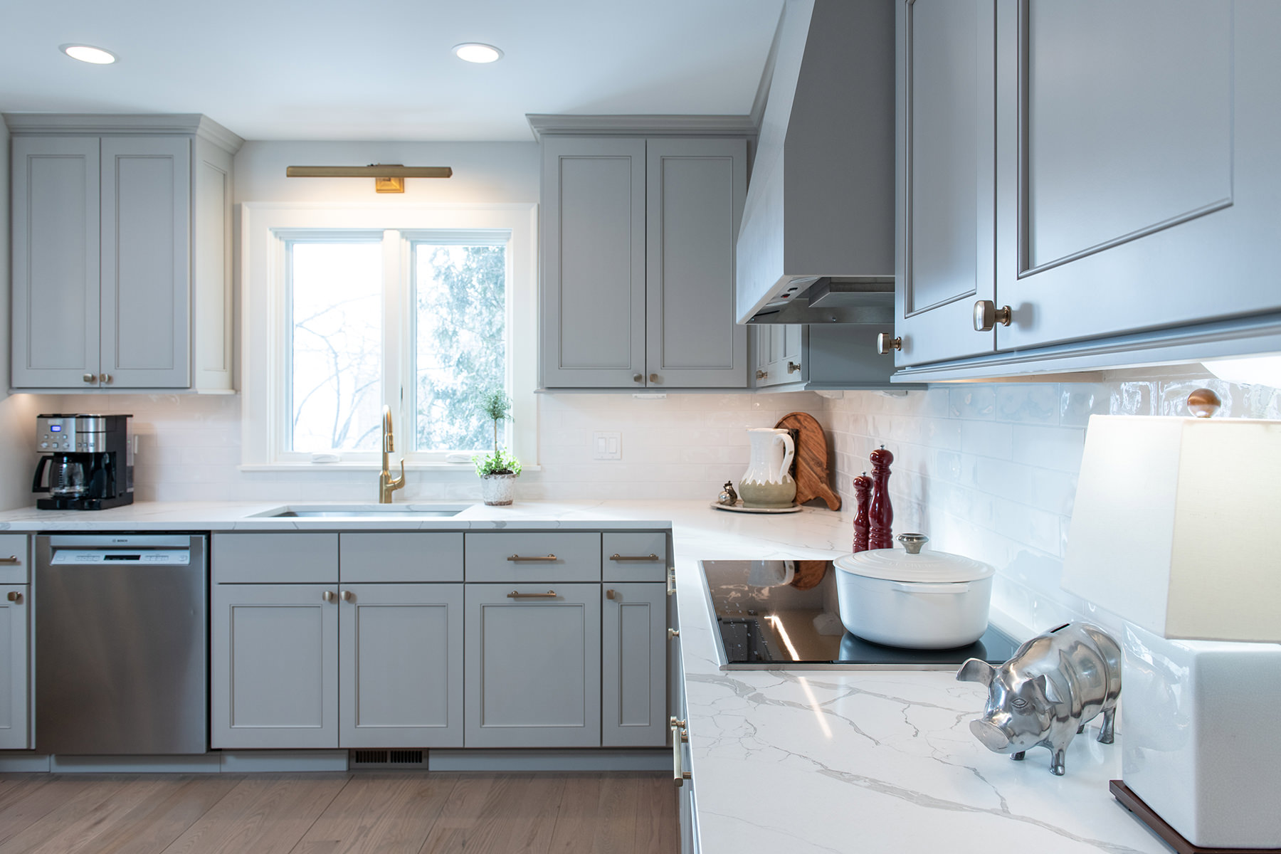 Remodeled home kitchen with white counter tops, light gray custom kitchen cabinets and champagne bronze kitchen hardware.