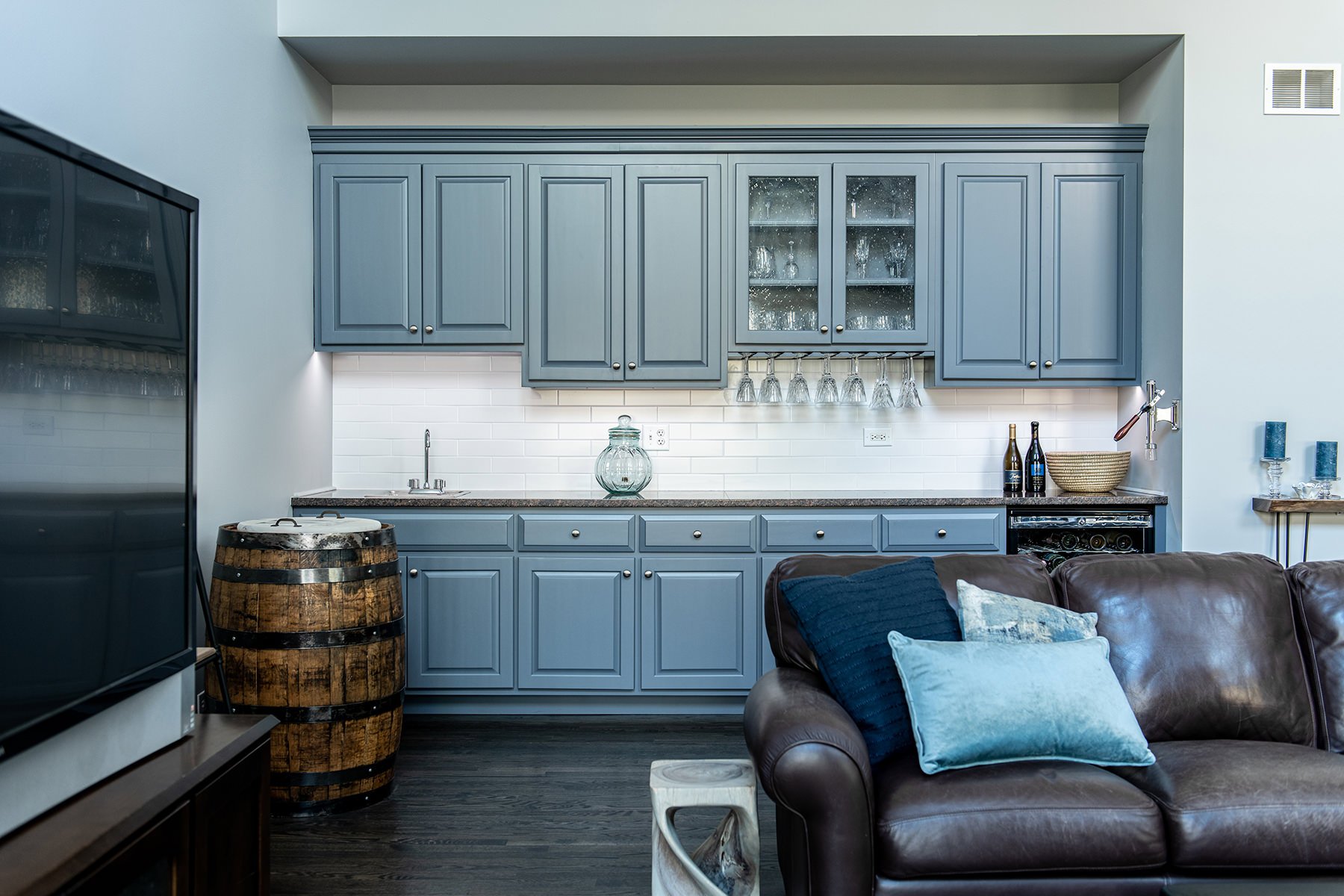Gray-blue cabinetry remodel with brown couch and dark wood floors.