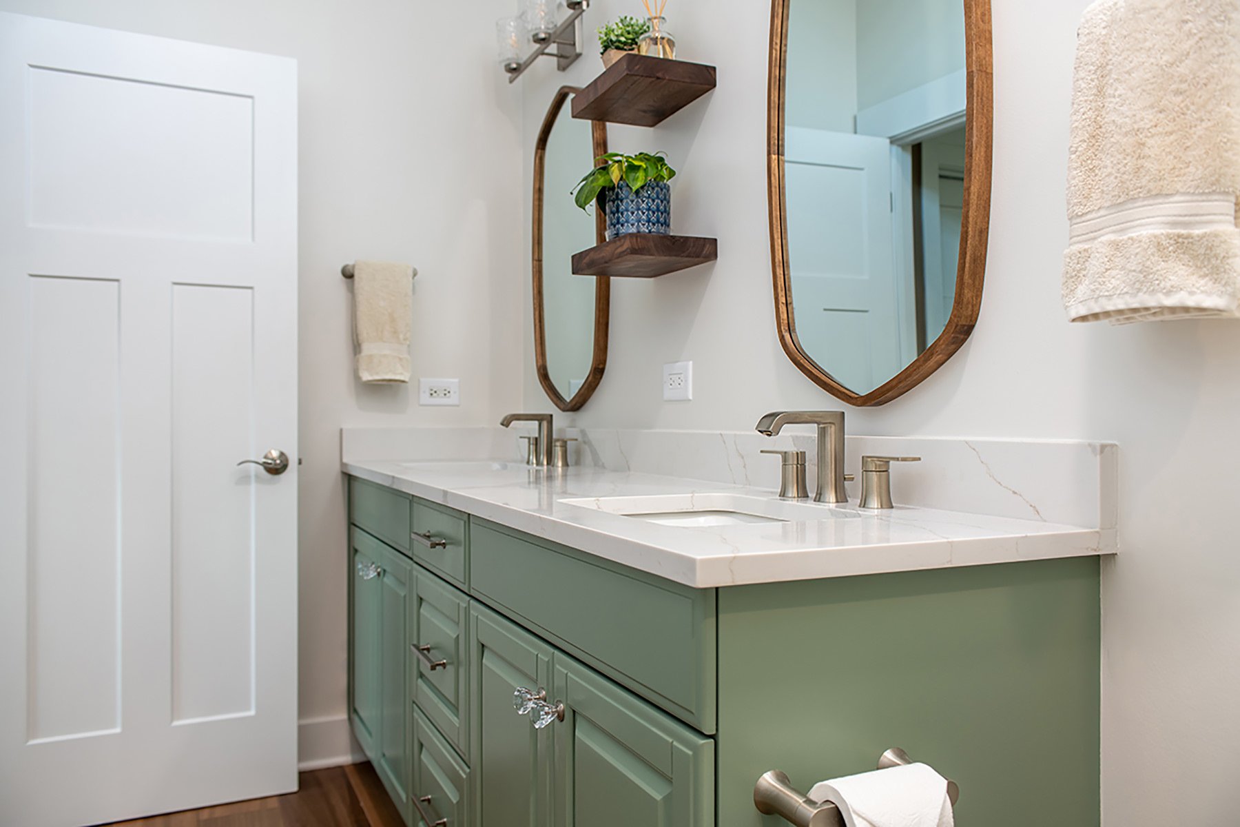 Remodeled primary bathroom with sage green painted cabinets and unique wood framed vanity mirrors and white countertops.