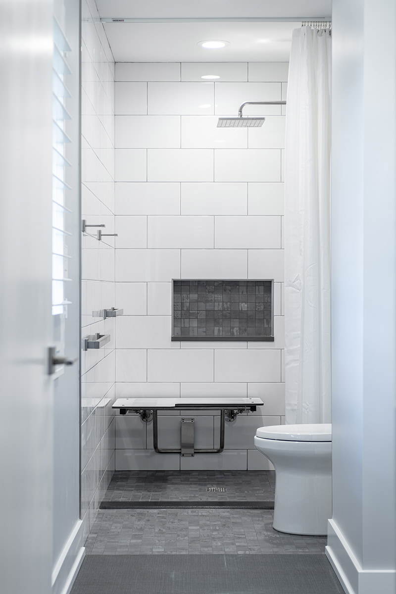 Bathroom shower with handicap accessibility features. White tile and dark gray inset tile.