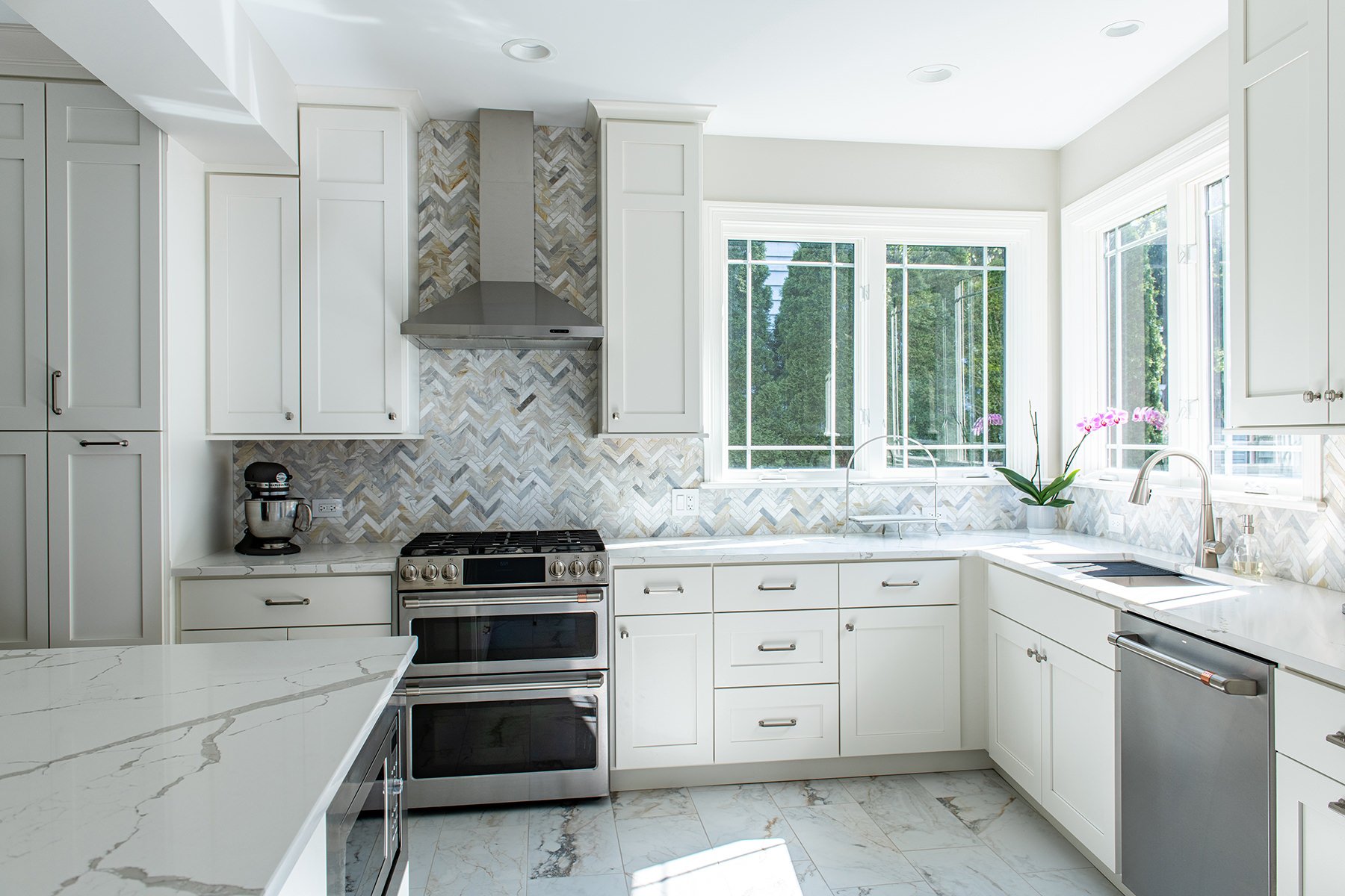 White kitchen with stainless steel appliances, herringbone backsplash and open natural lighting.