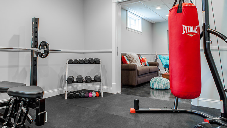 Remodeled room into a home gym with black rubber floors, free-weight rack, and a red boxing bag.